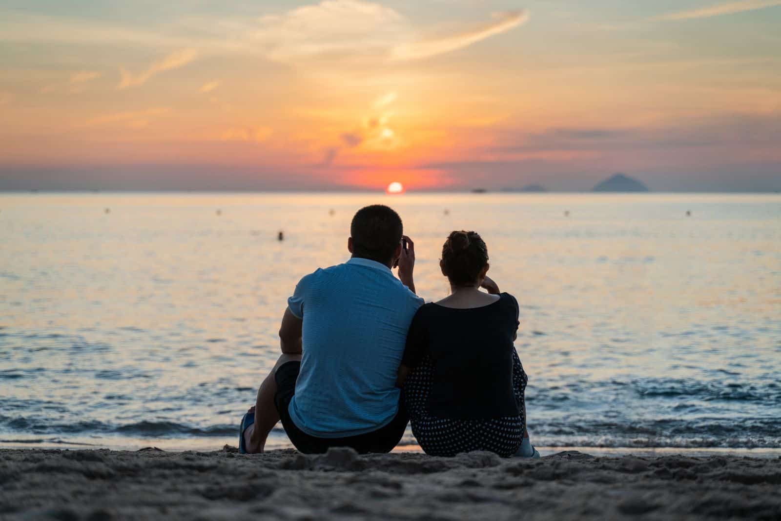 un homme et une femme sont assis sur la plage au bord de la mer