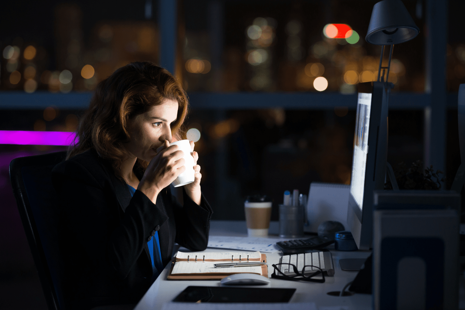 une femme est assise à une table en train de boire du café tout en travaillant