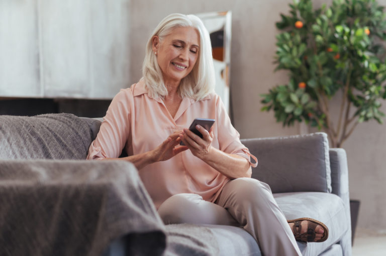 femme plus âgée assise sur un canapé envoyant des SMS