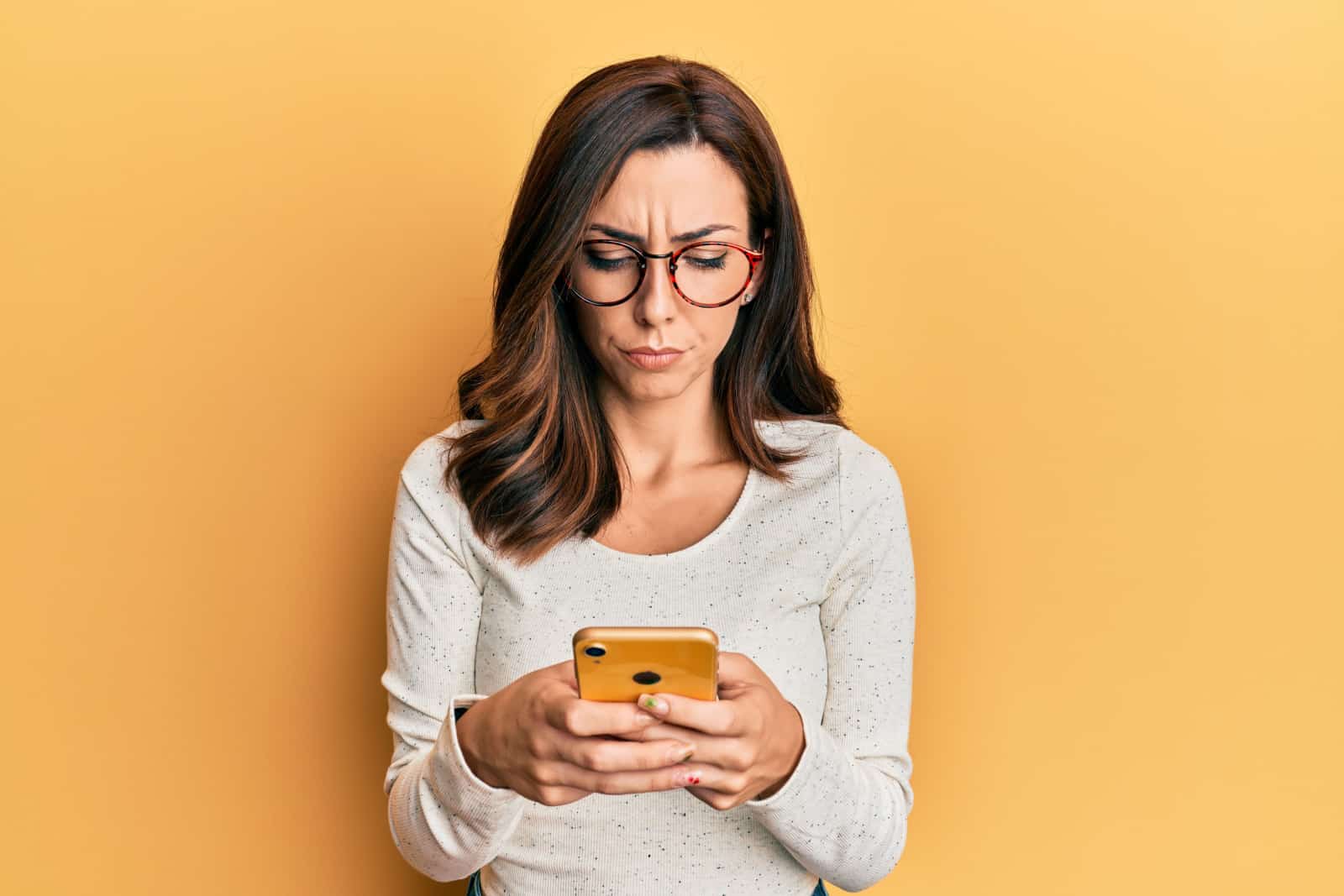 femme brune tape au téléphone avec une expression confuse, fond orange
