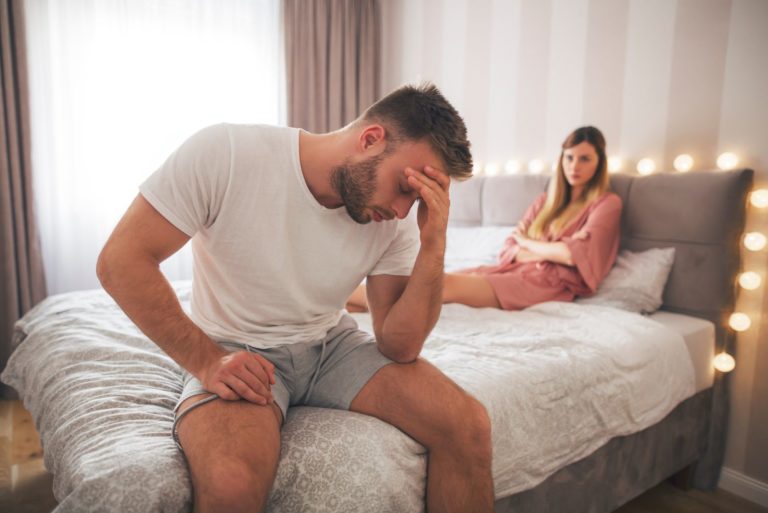 un homme déçu est assis sur le lit tandis qu'une femme est assise sur lui