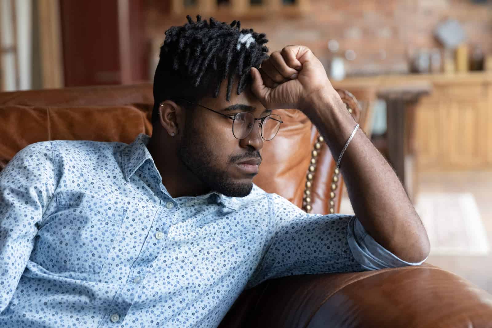 Jeune homme d'origine africaine frustré dans des verres assis sur un canapé, pensant ou problèmes de vie