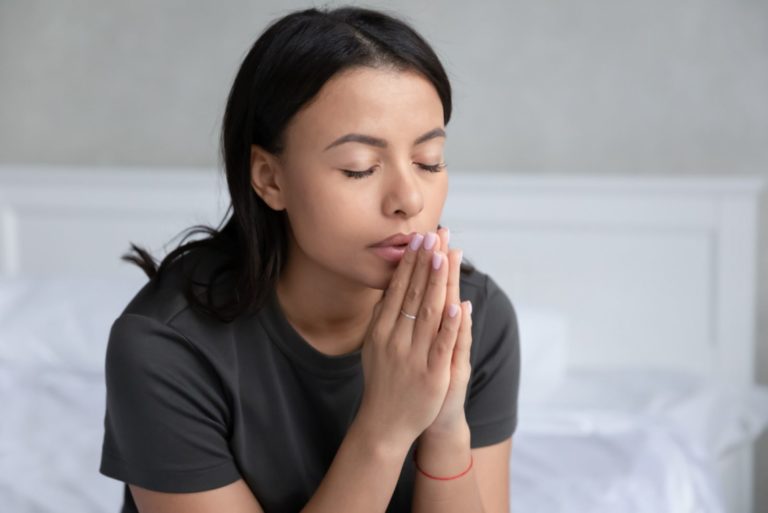 jeune femme assise sur le lit dans la chambre tenant la main en prière