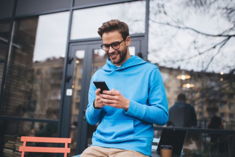 un homme souriant se tient dans la rue et tape au téléphone