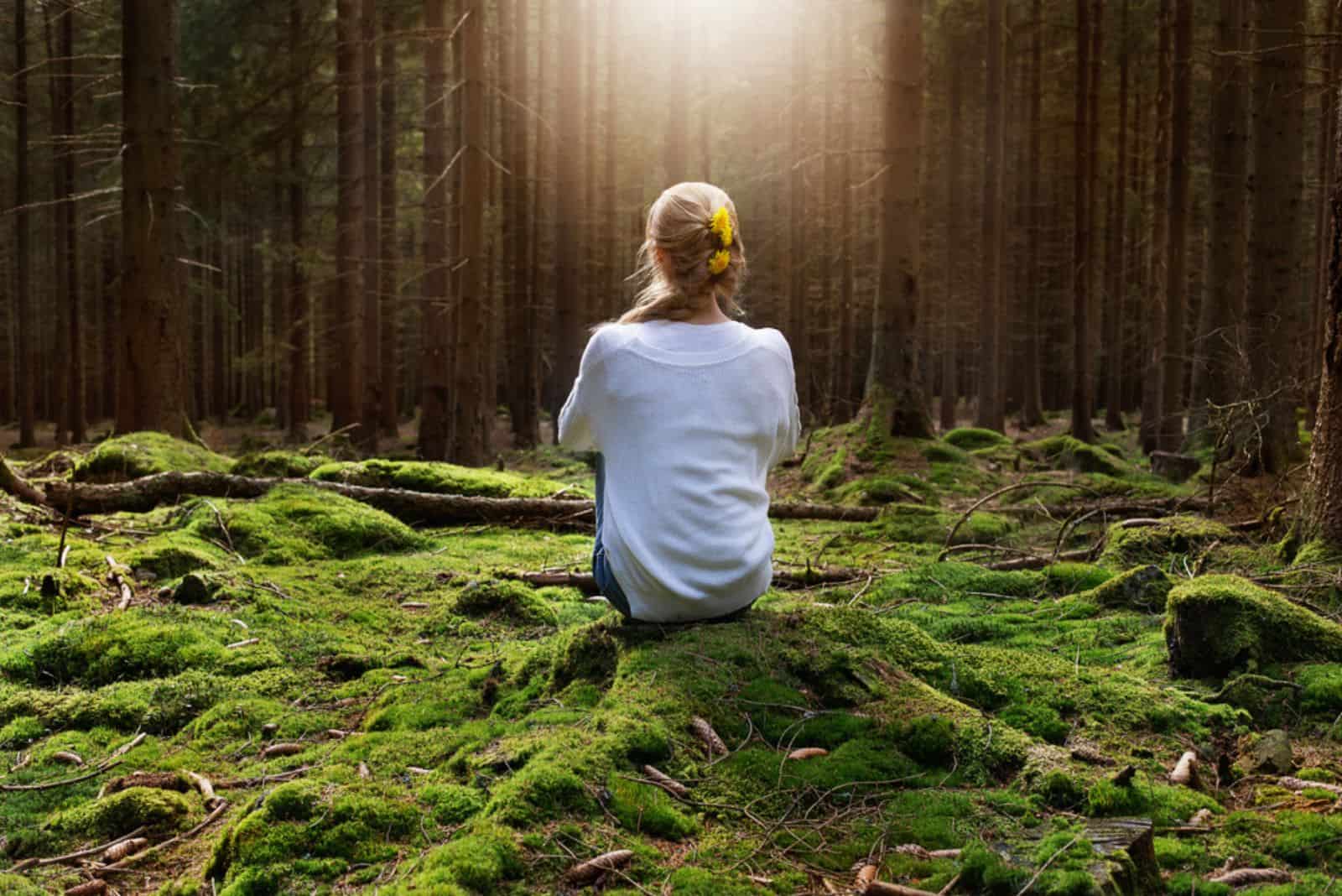 Une femme assise dans la forêt apprécie le silence et la beauté de la nature.