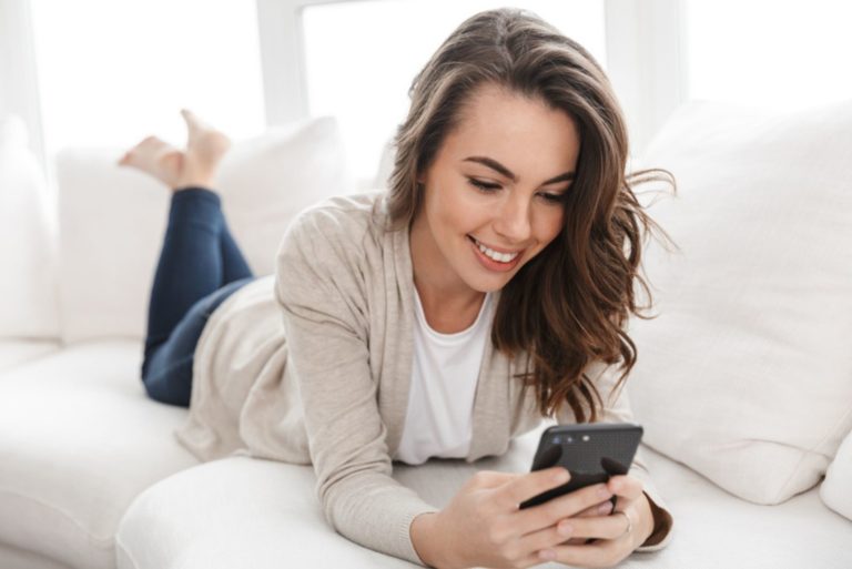une belle fille est allongée sur le lit et tape au téléphone