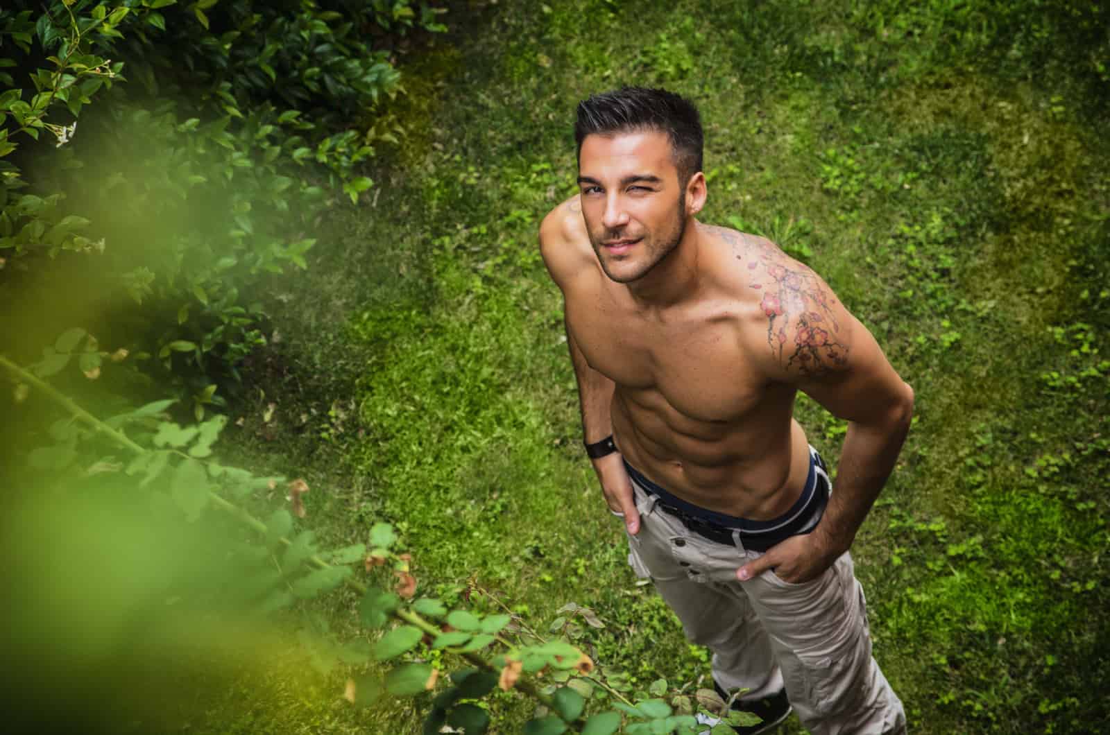 homme chaud debout sur l'herbe avec un clin d'œil à la caméra