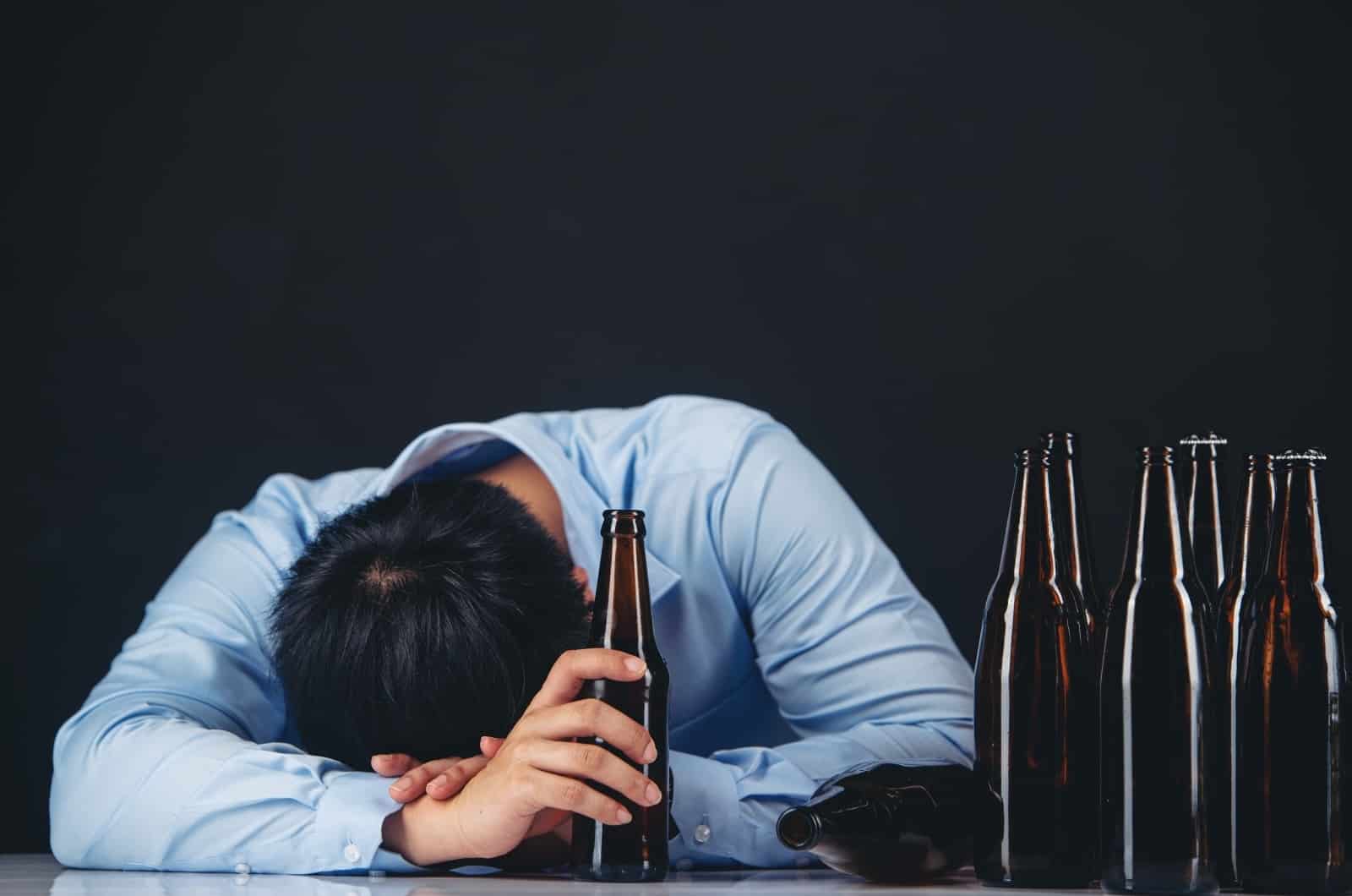 homme ivre dormant sur une table avec des bouteilles dessus