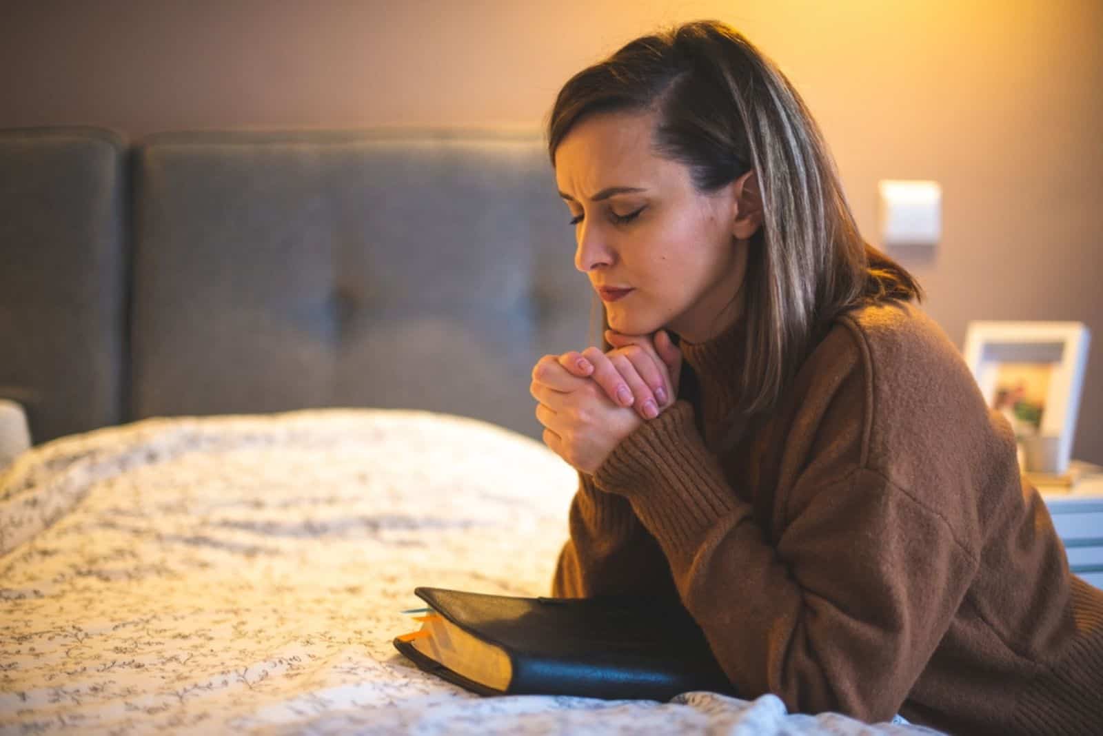 jeune femme priant au-dessus du lit avec bible