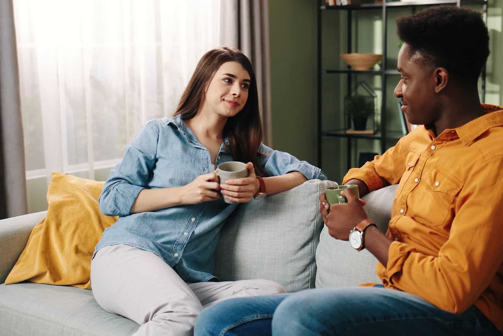 un homme et une femme sont assis sur le canapé avec du café et parlent