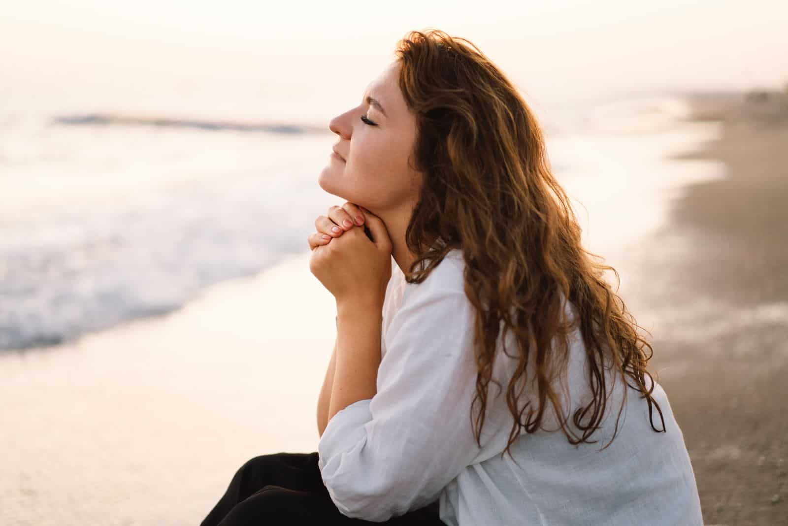 une belle femme aux longs cheveux bruns est assise sur la plage et prie