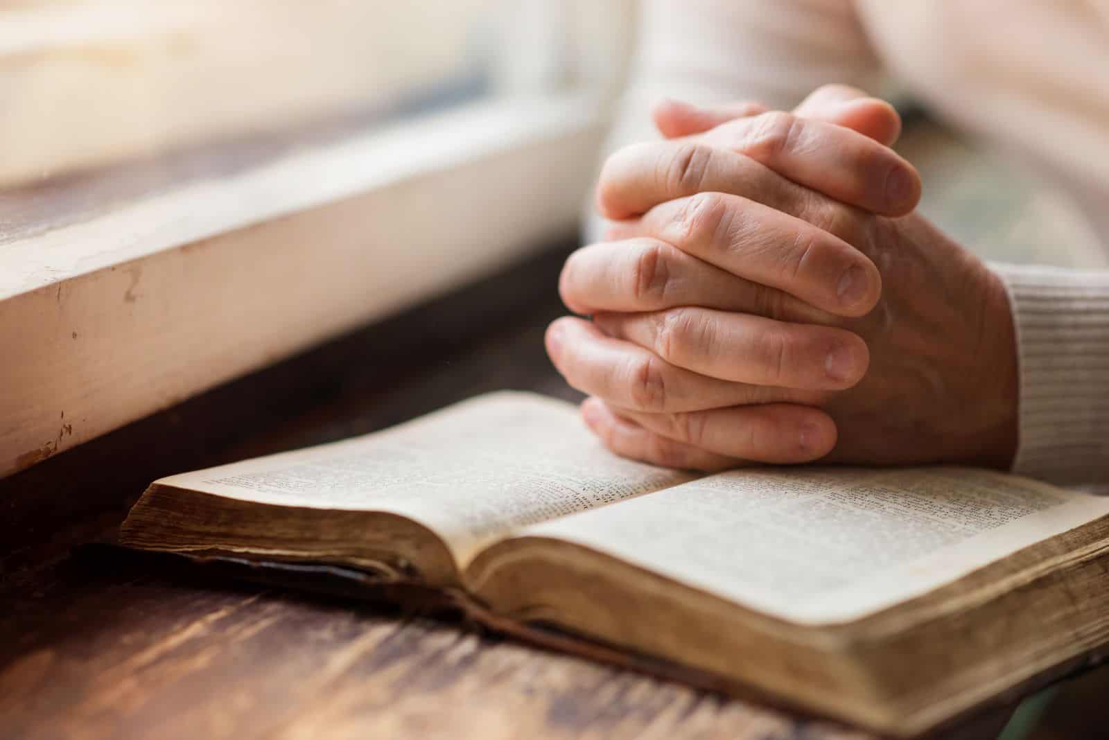 une femme avec ses mains posées sur un livre prie