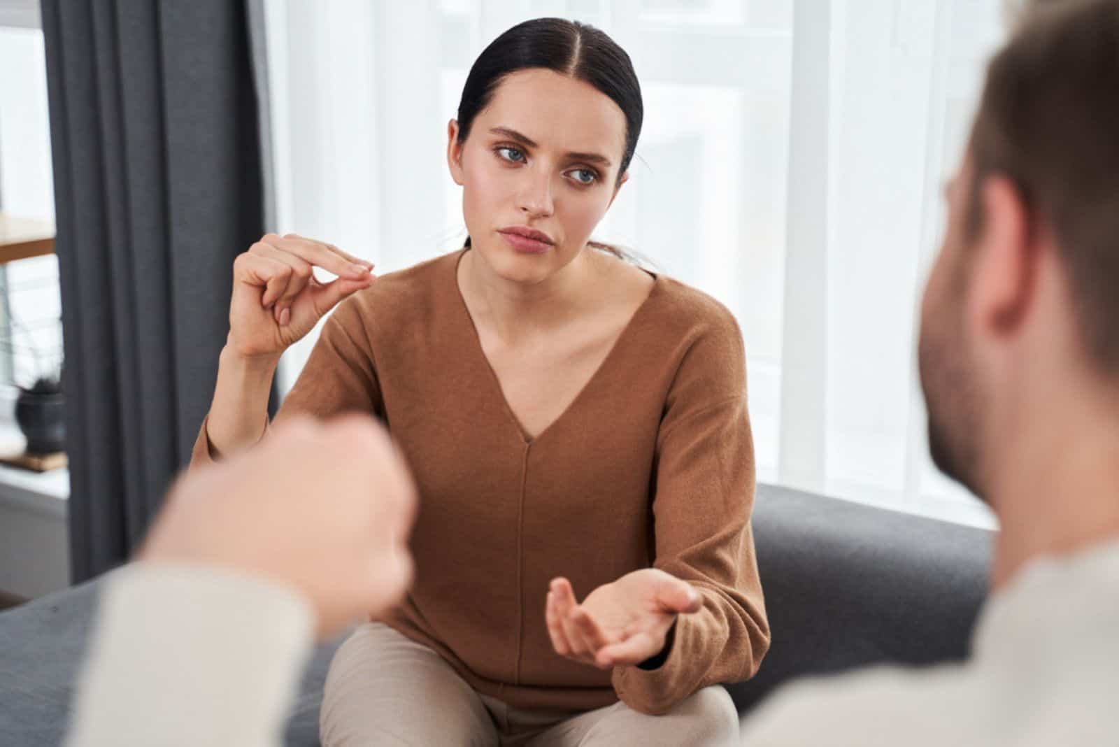 une femme pensive est assise sur le canapé et parle à un homme