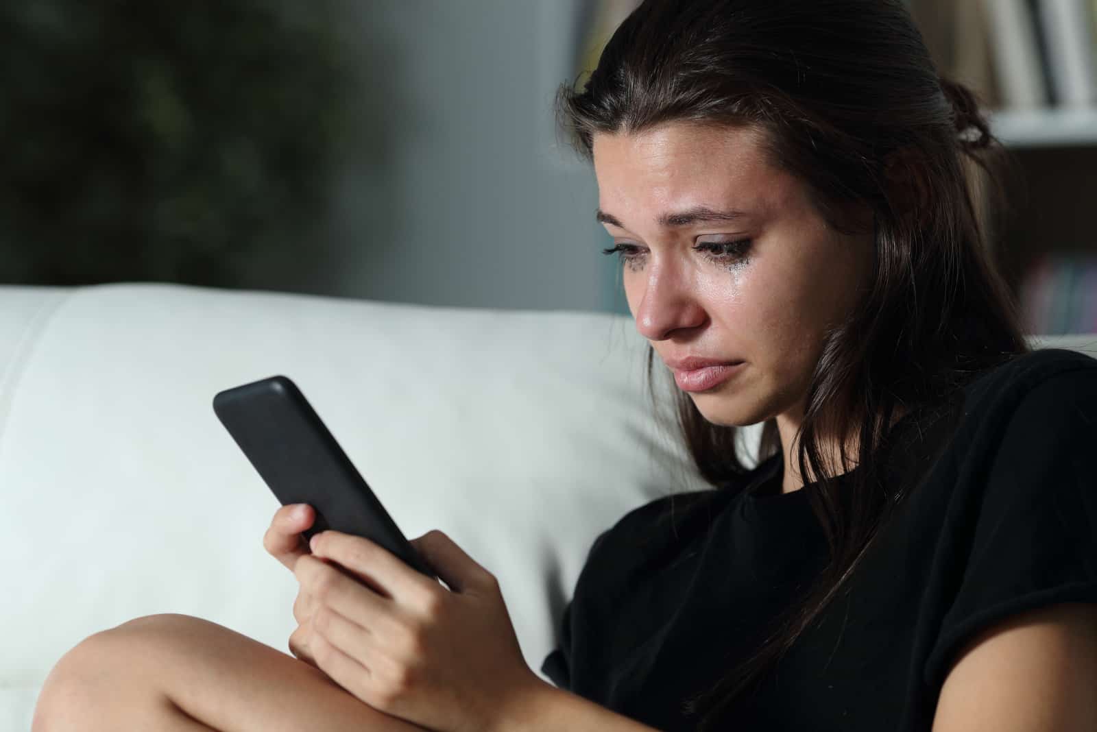 une femme triste pleure beaucoup et regarde son téléphone, se demandant si elle devrait bloquer son ex