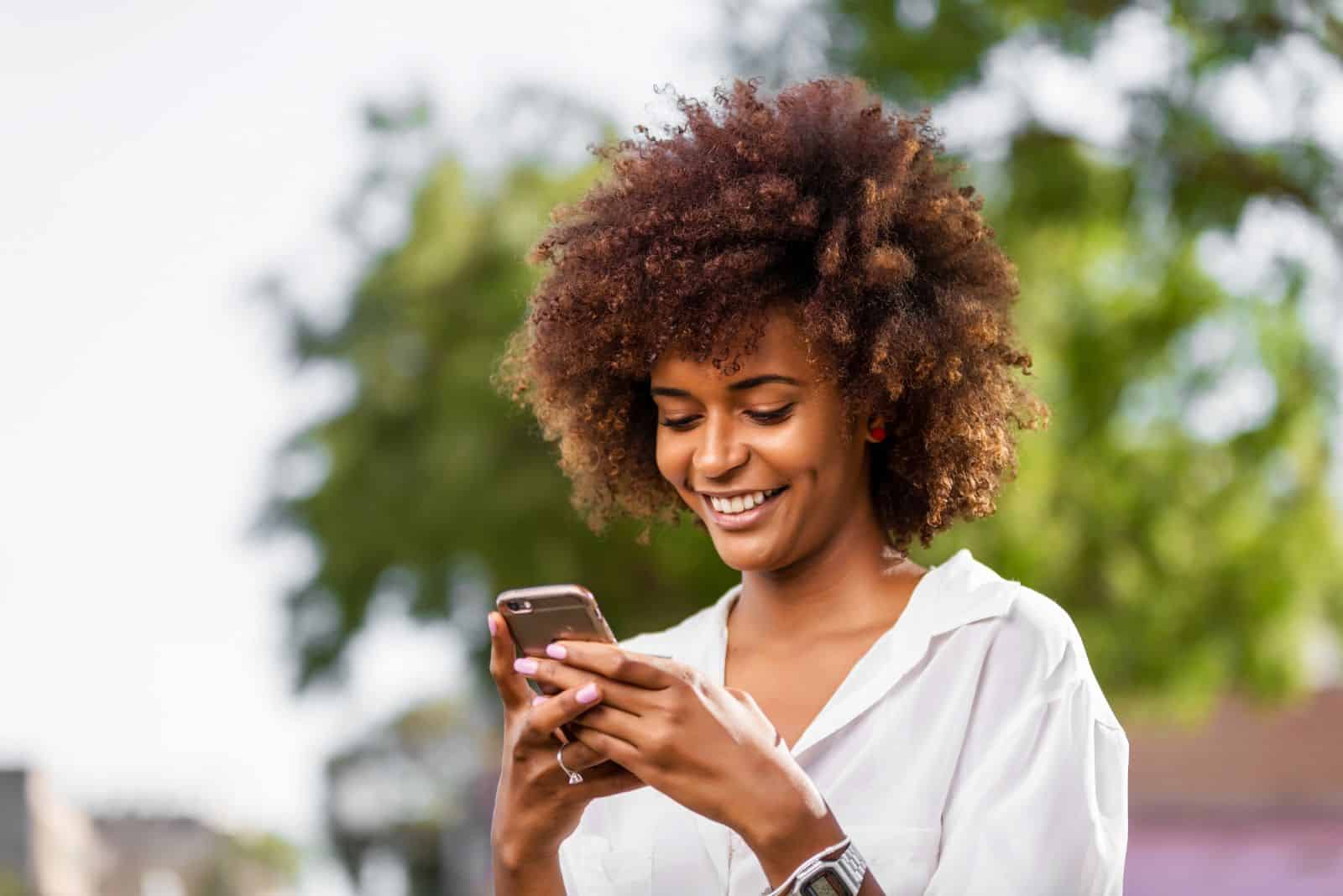 une fille souriante aux cheveux ébouriffés tient un téléphone portable dans sa main