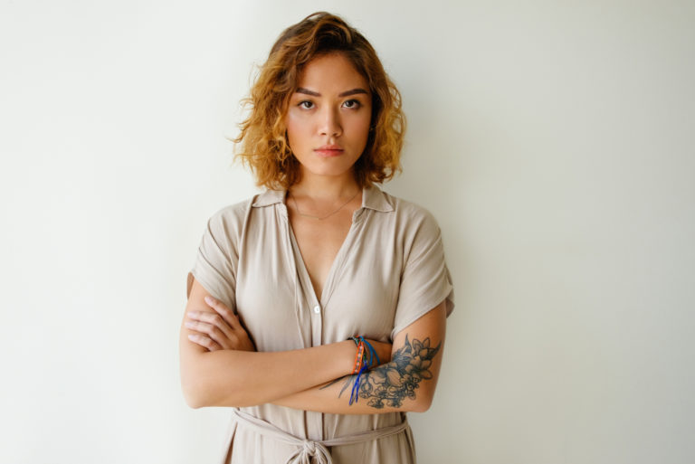 femme tatouée avec les bras croisés fait une expression agacée