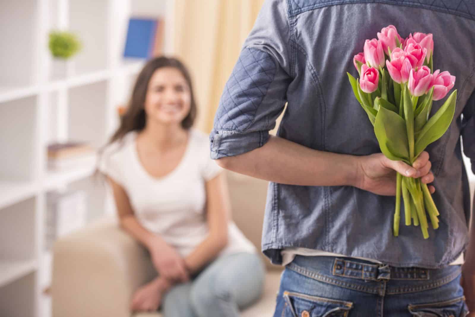 Guy tient une fleur derrière lui et essaie de surprendre sa petite amie qui attend à la maison