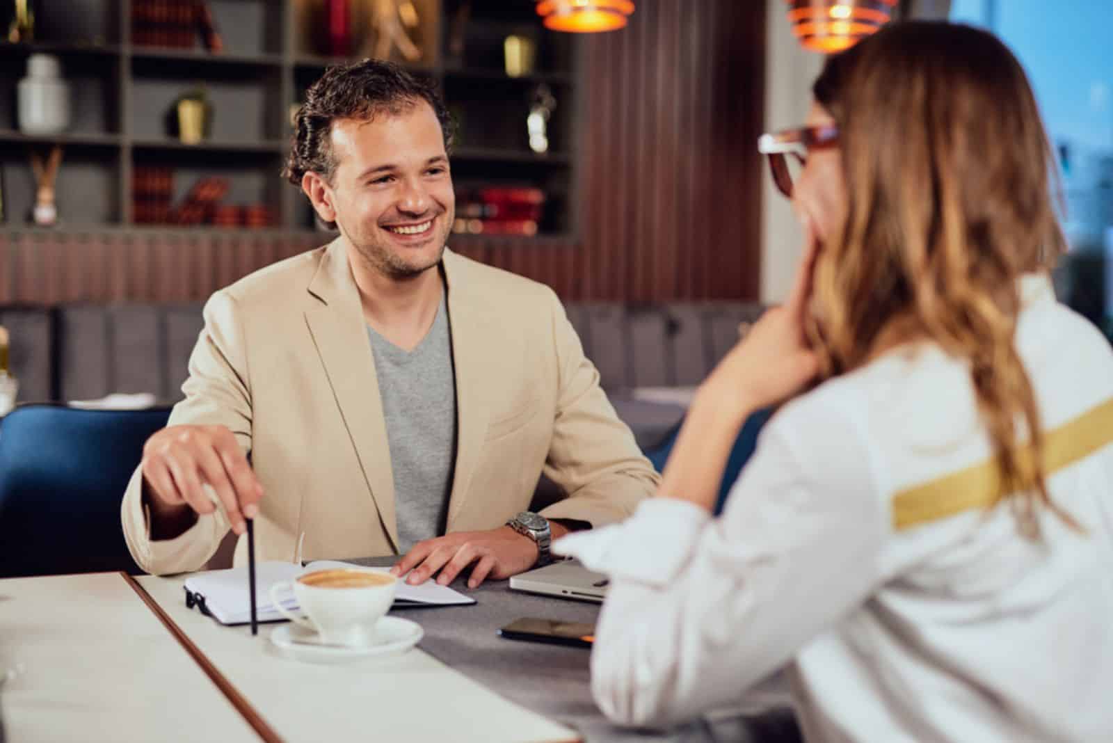 un homme souriant est assis à une table avec une femme et ils parlent