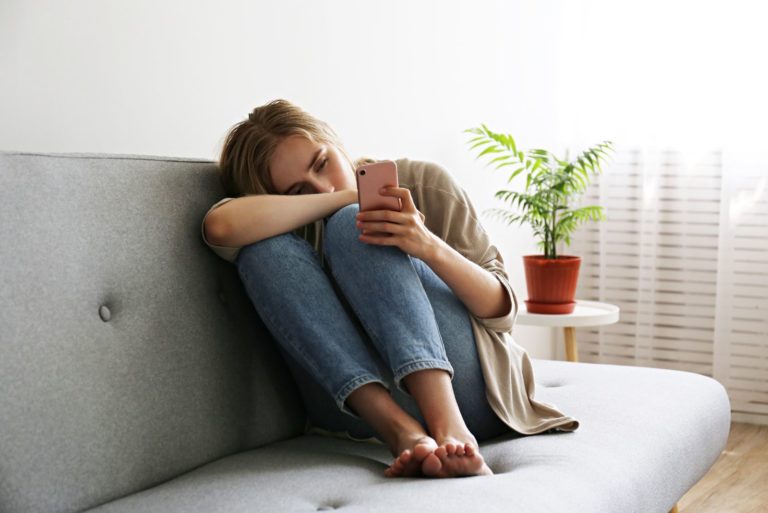 fille triste assise sur le canapé et tapant au téléphone