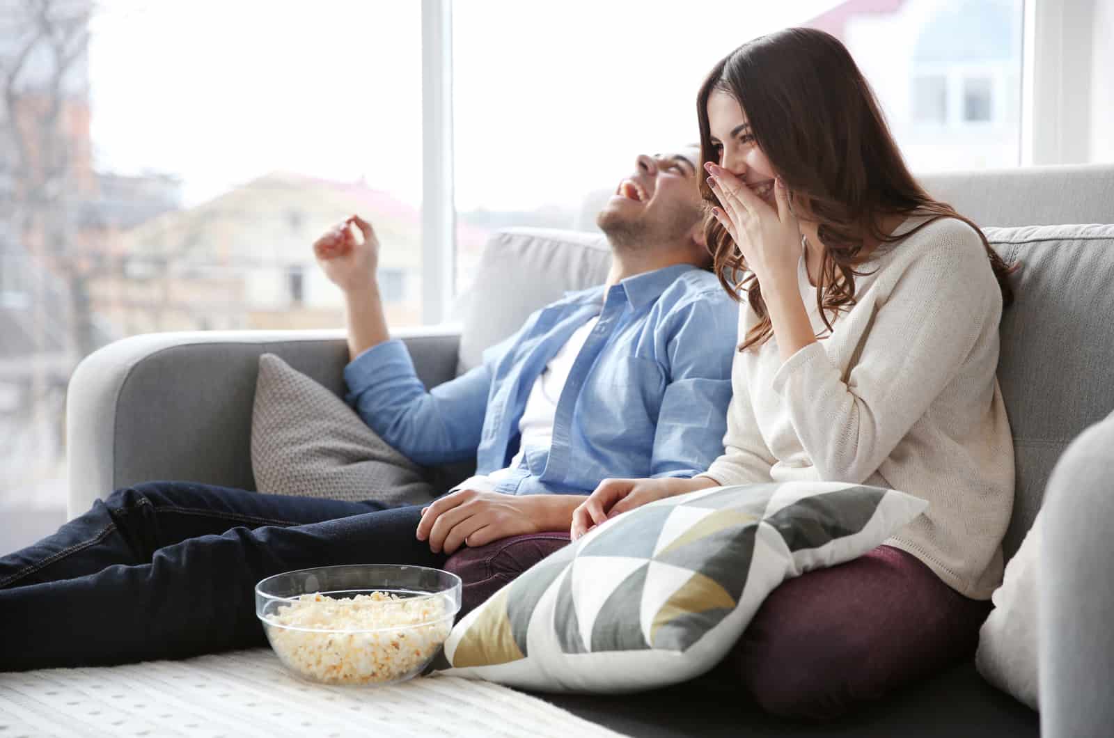 couple riant en mangeant du pop-corn sur le canapé