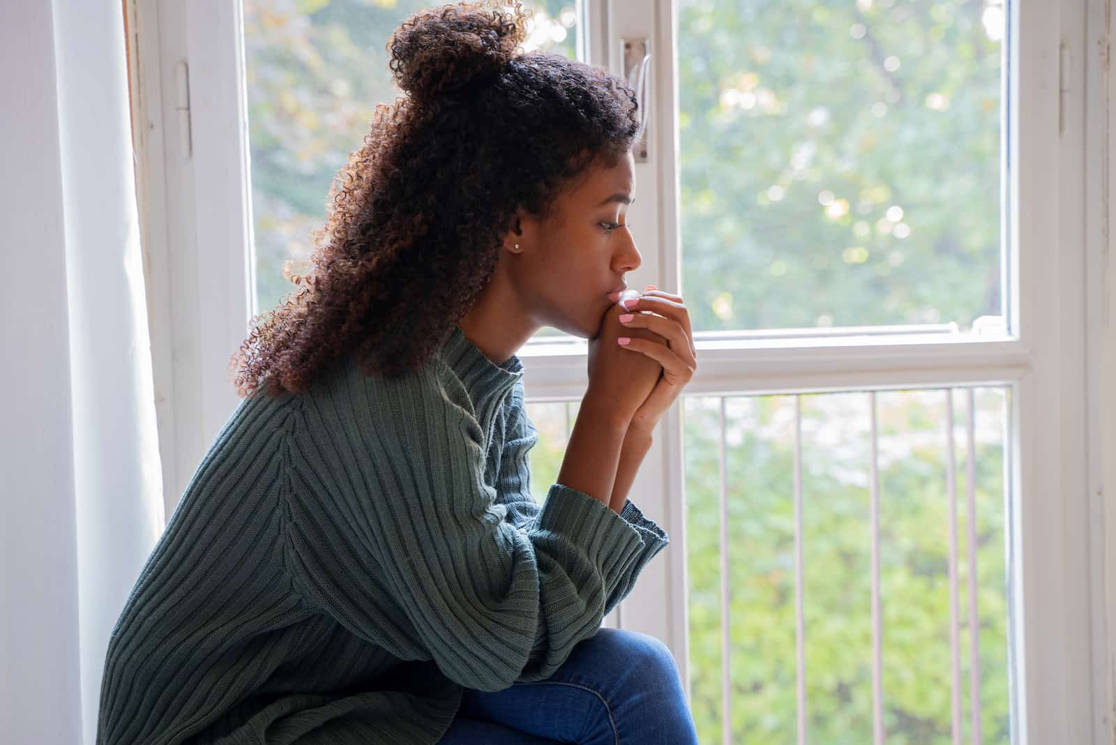 fille assise près de la fenêtre priant