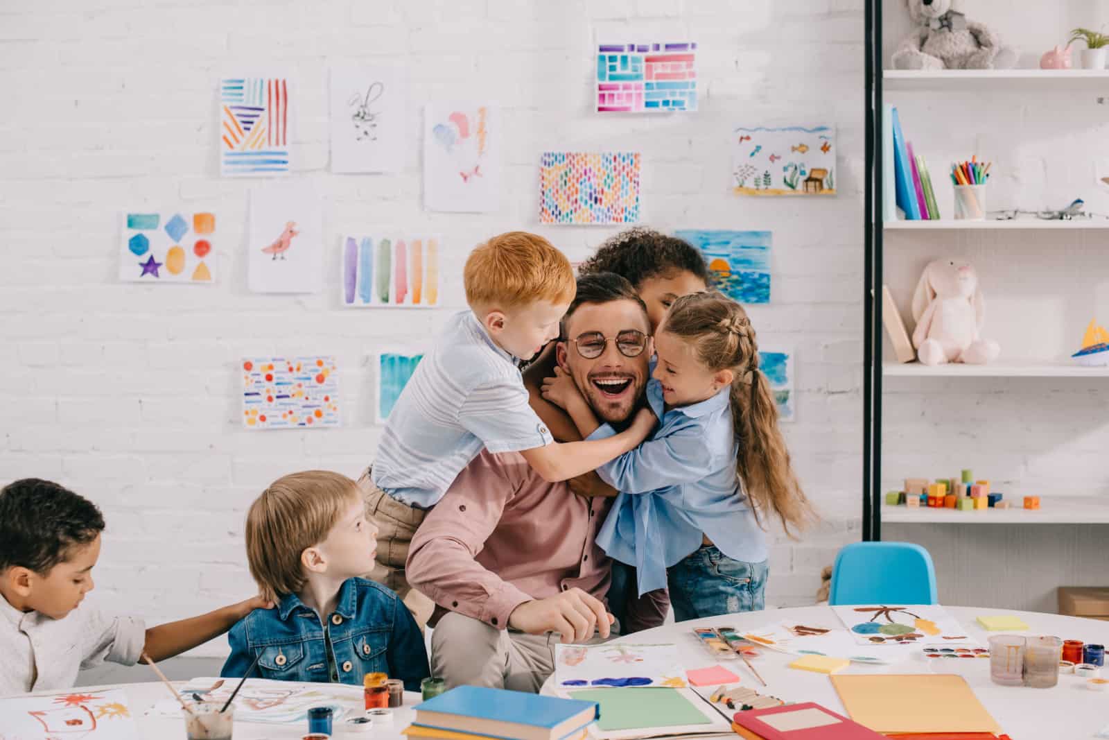 les enfants embrassent un enseignant heureux à table dans la salle de classe