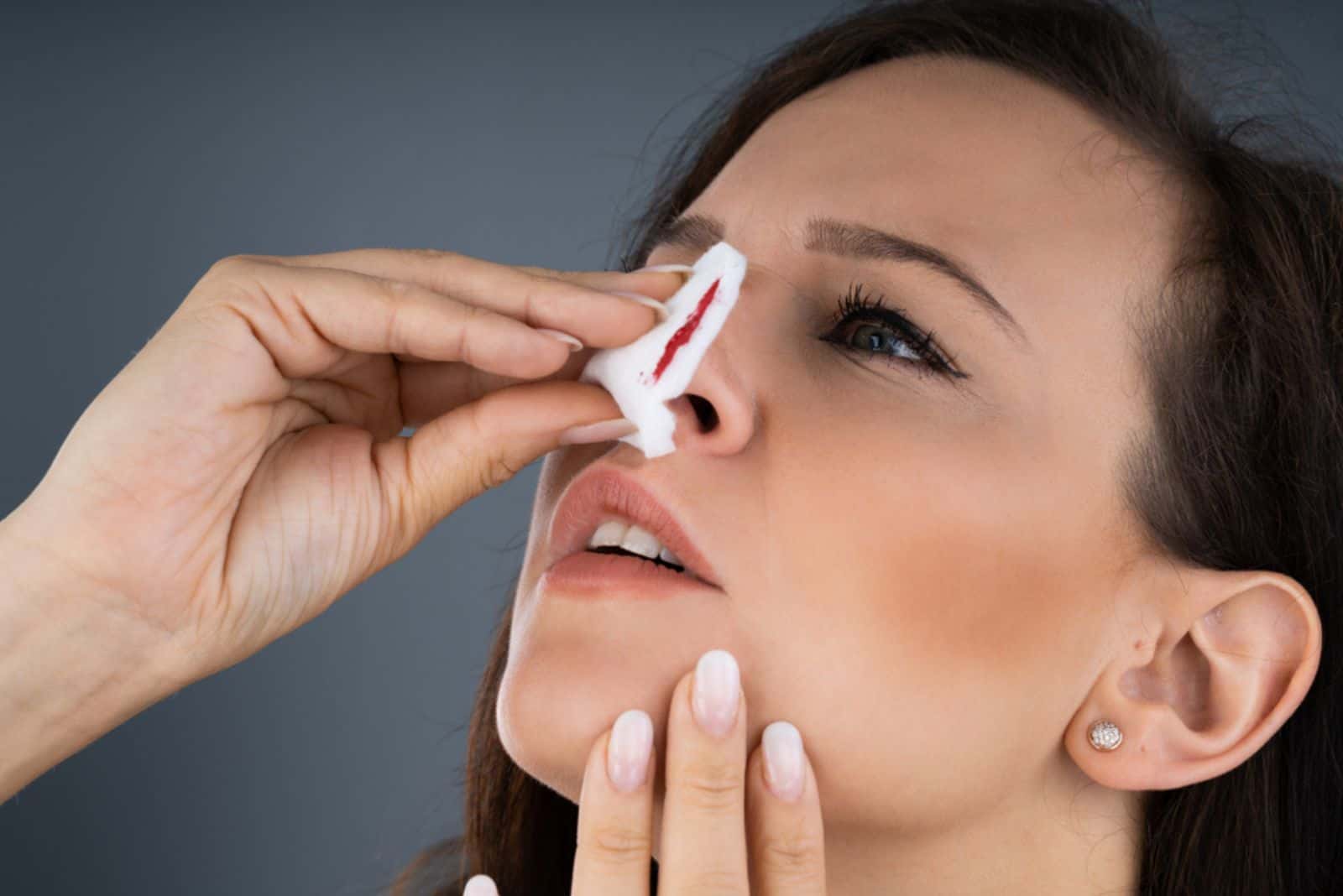 une femme met une boule de coton sur son nez pendant qu'il saigne