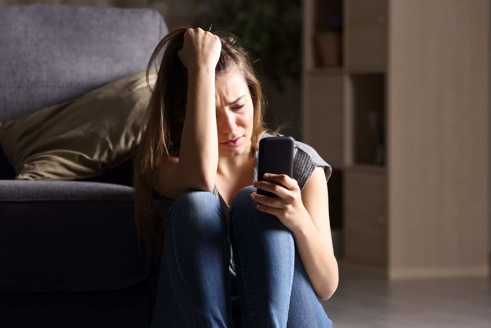 une fille qui pleure est assise par terre et tape au téléphone