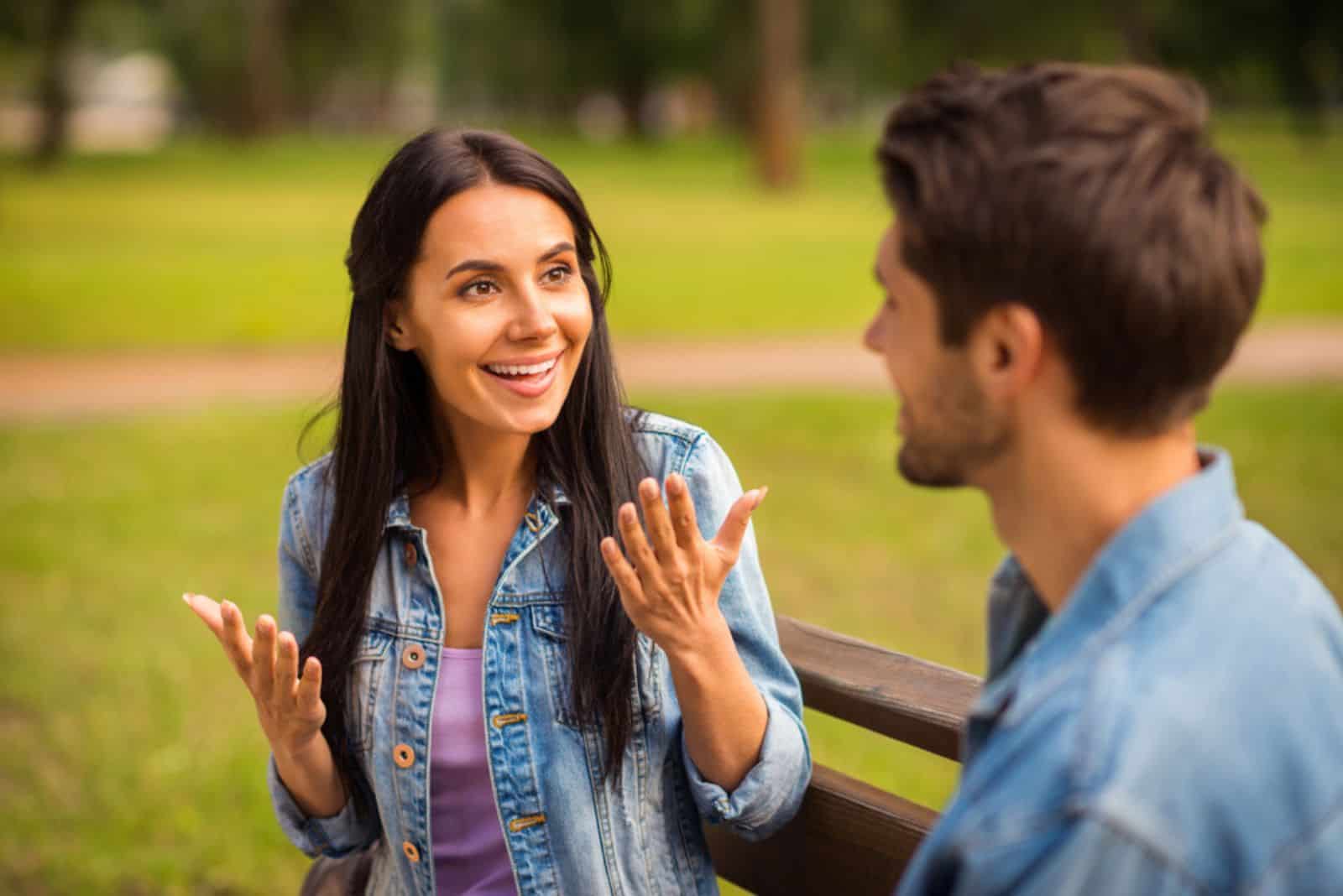 une fille souriante aux longs cheveux noirs parle à un homme sur un banc de parc