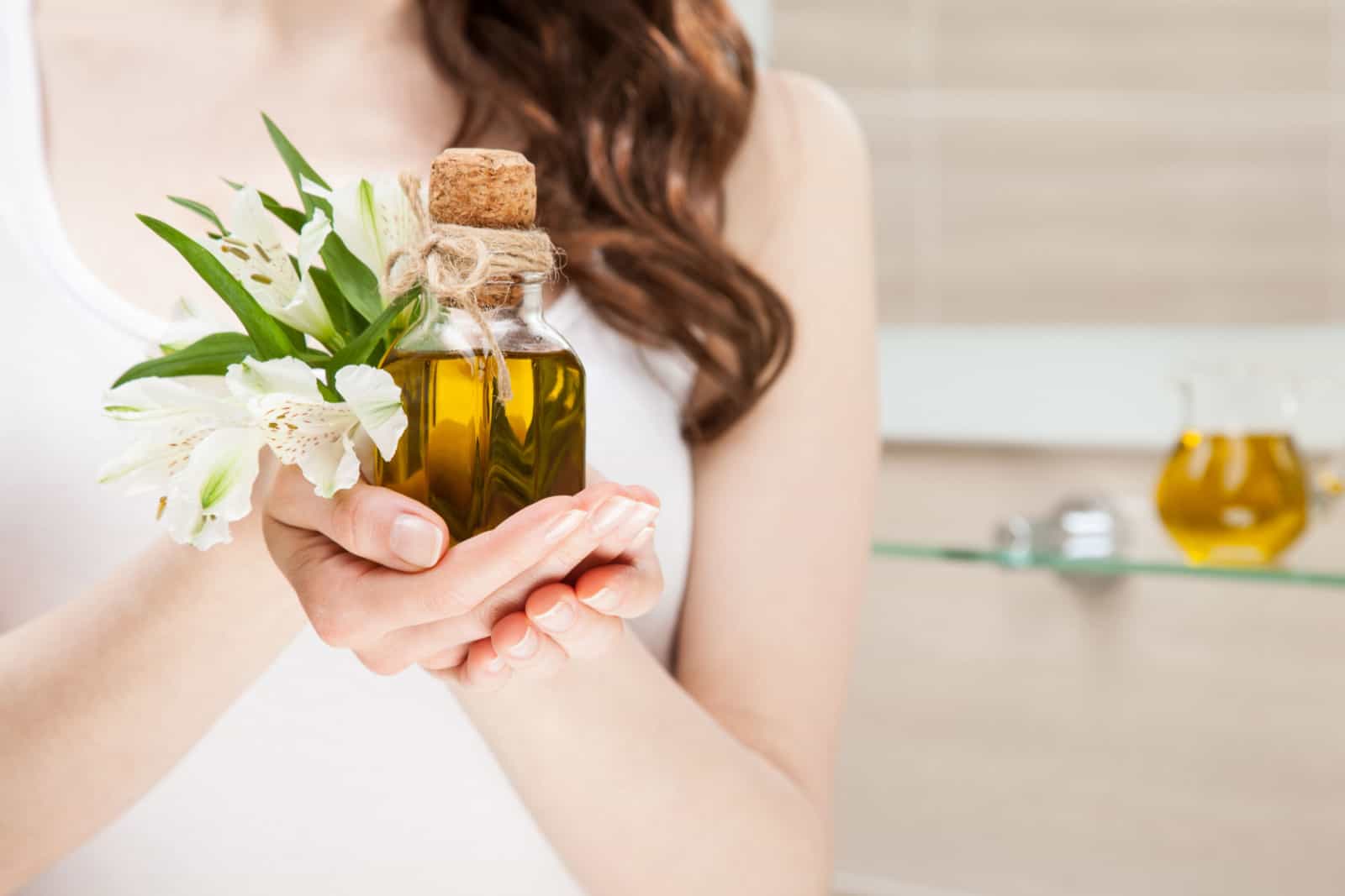Femme méconnaissable tenant une bouteille d'huile d'olive naturelle et de belles fleurs fraîches