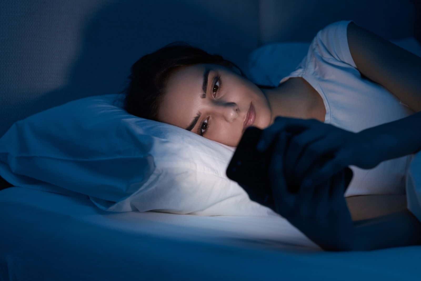 Jeune femme allongée dans son lit et naviguant sur les réseaux sociaux