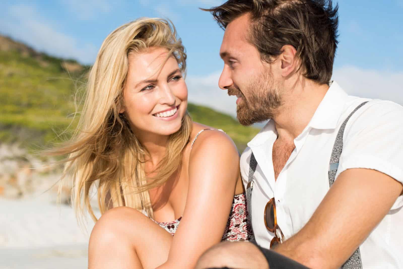 couple d'amoureux souriant assis sur la plage et parler