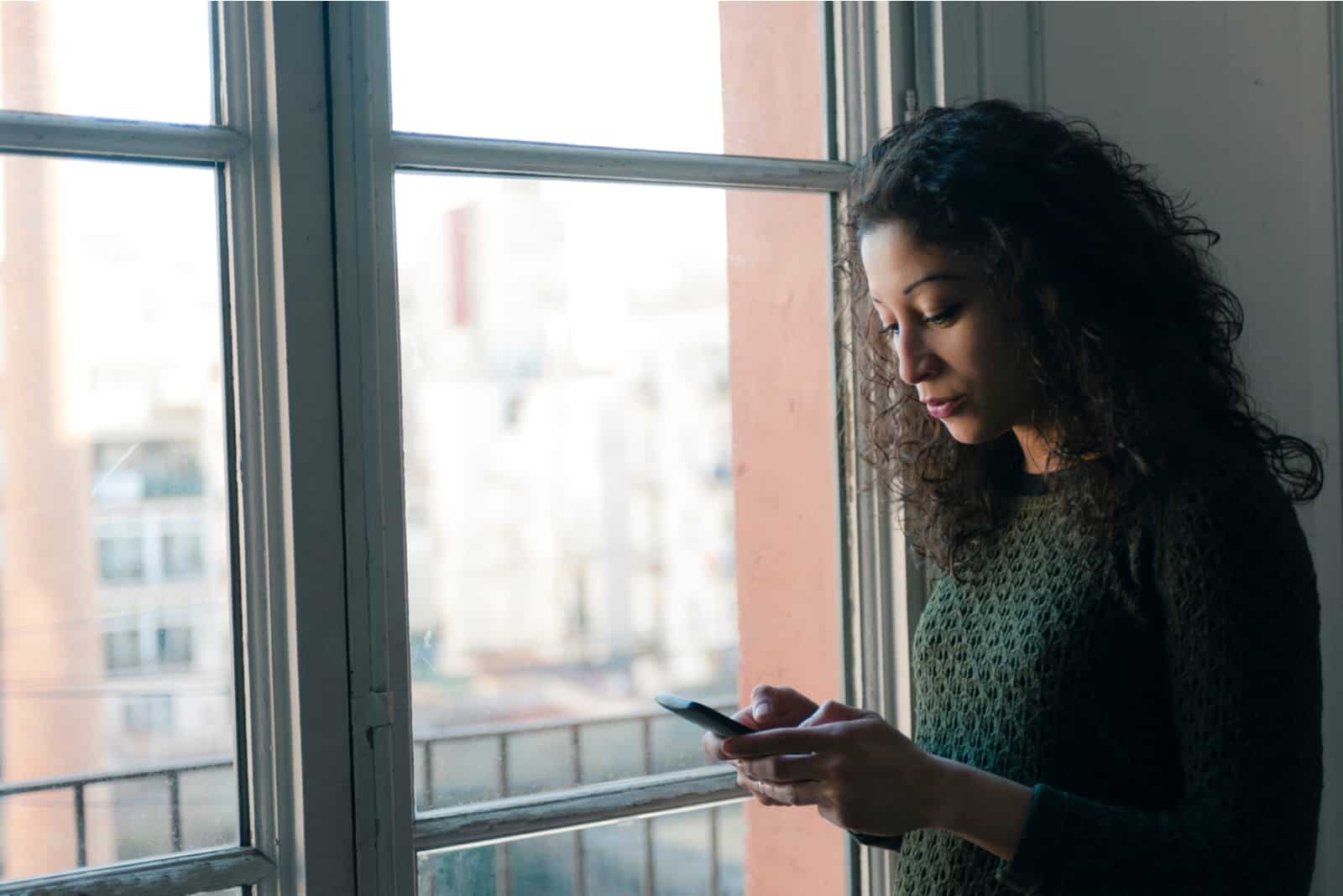 femme debout près d'une fenêtre et tapant au téléphone