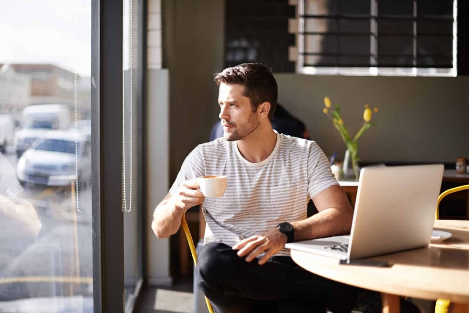 un homme est assis pensivement dans un café et regarde par la fenêtre