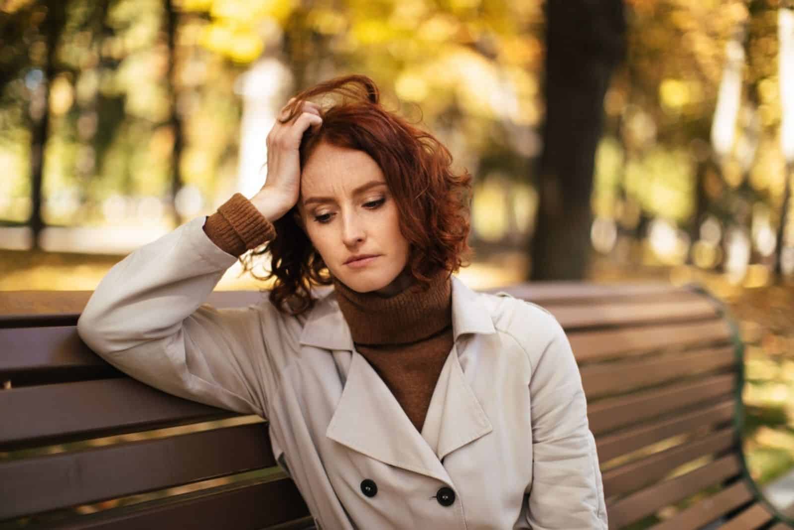 une fille pensive est assise sur un banc de parc