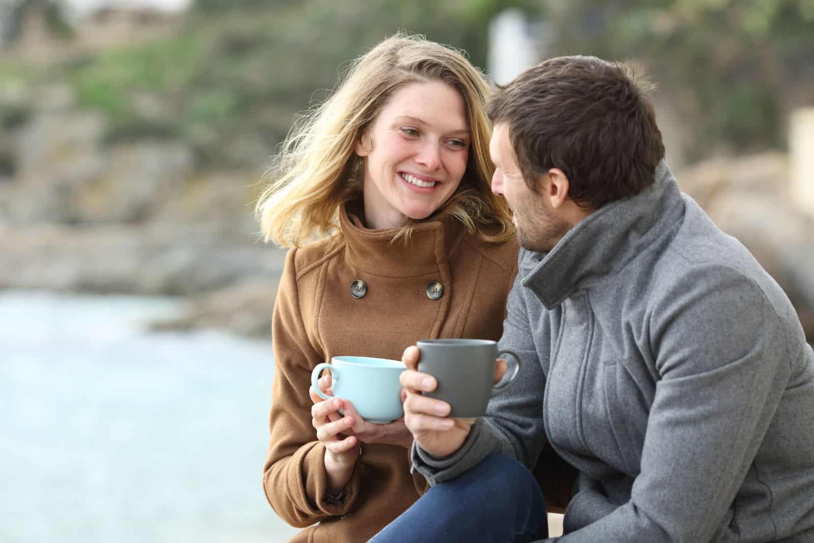 une fille souriante est assise à côté d'un homme sur la plage et ils parlent