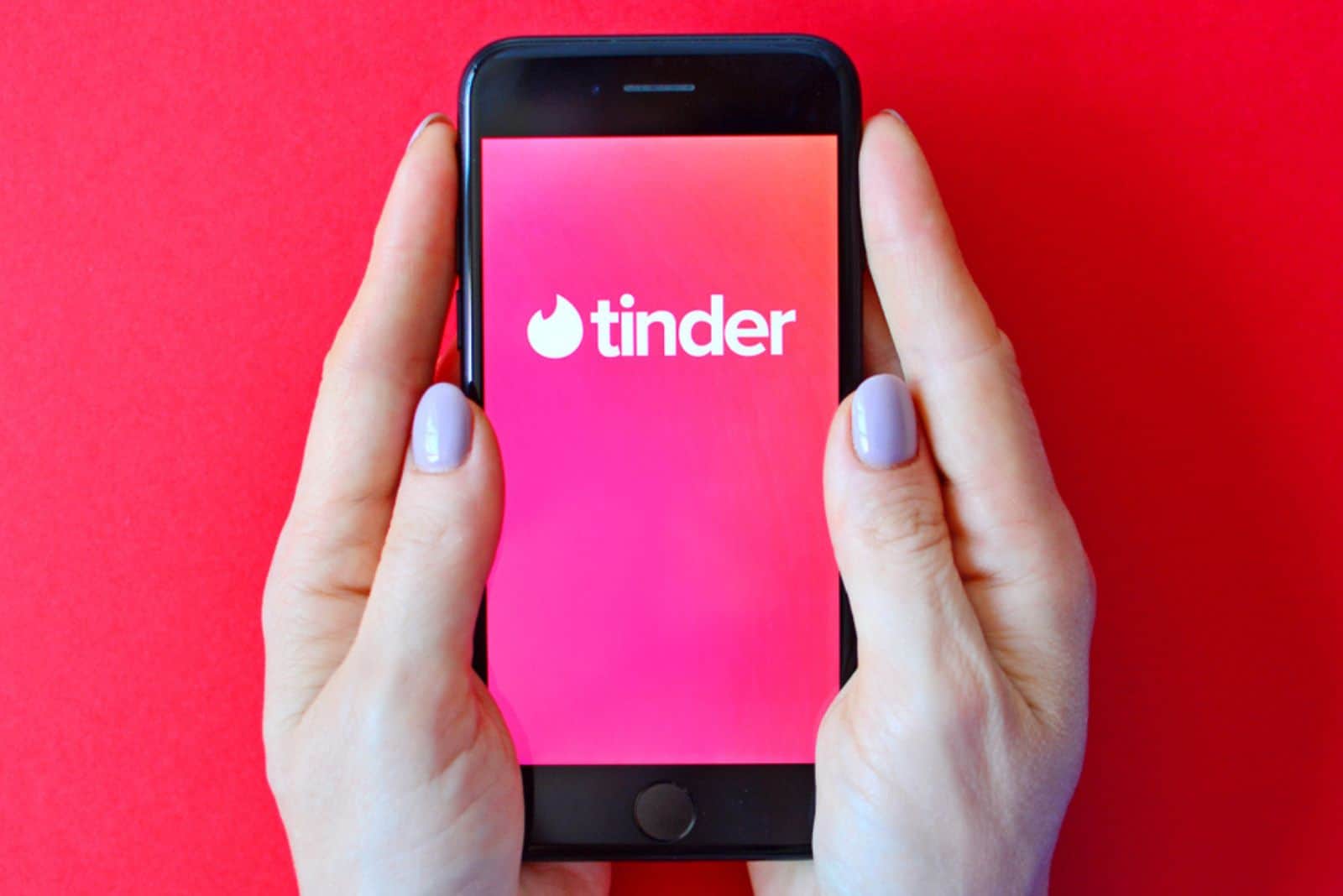 Éditorial illustratif du logo Tinder sur l'écran du smartphone dans les mains des femmes.