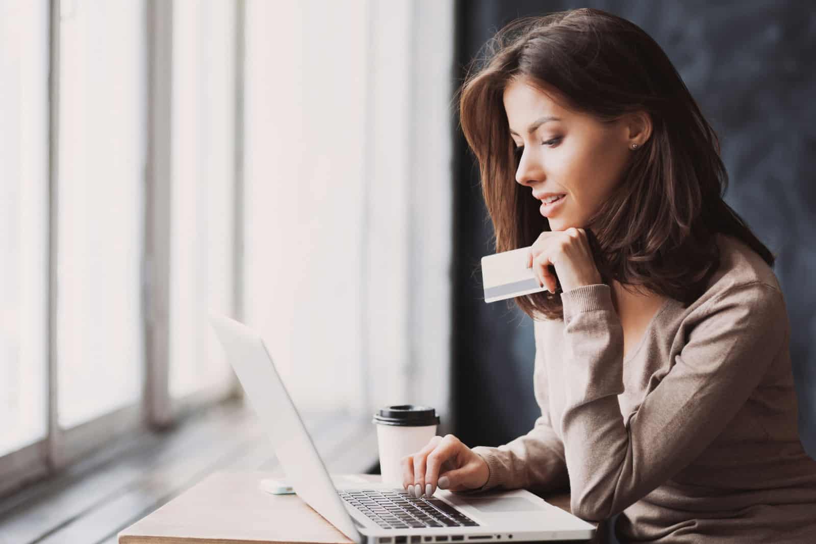 Jeune femme tenant une carte de crédit et utilisant un ordinateur portable.