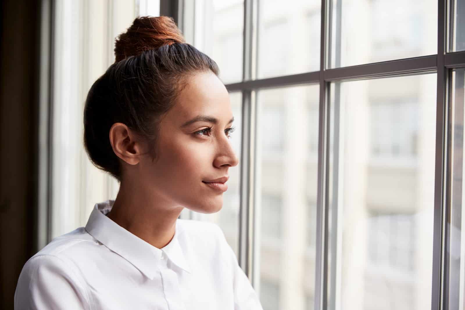 femme portant une chemise blanche et regardant par la fenêtre