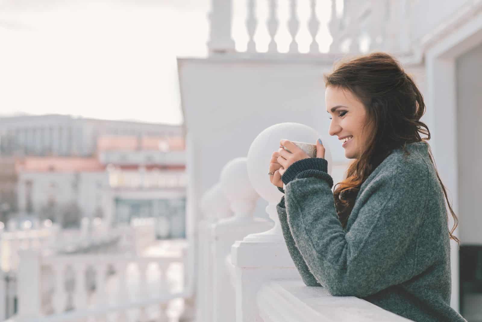 jeune fille souriante s'appuyant sur le balcon avec une tasse à la main