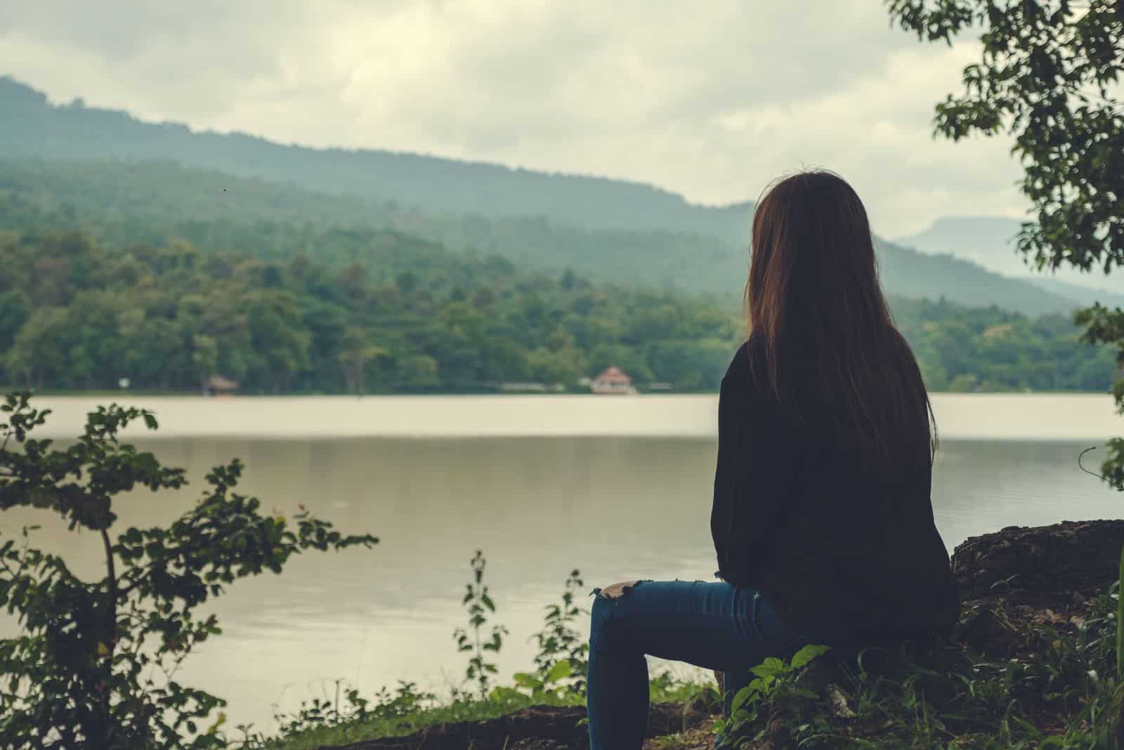 une fille aux longs cheveux bruns est assise au bord du lac