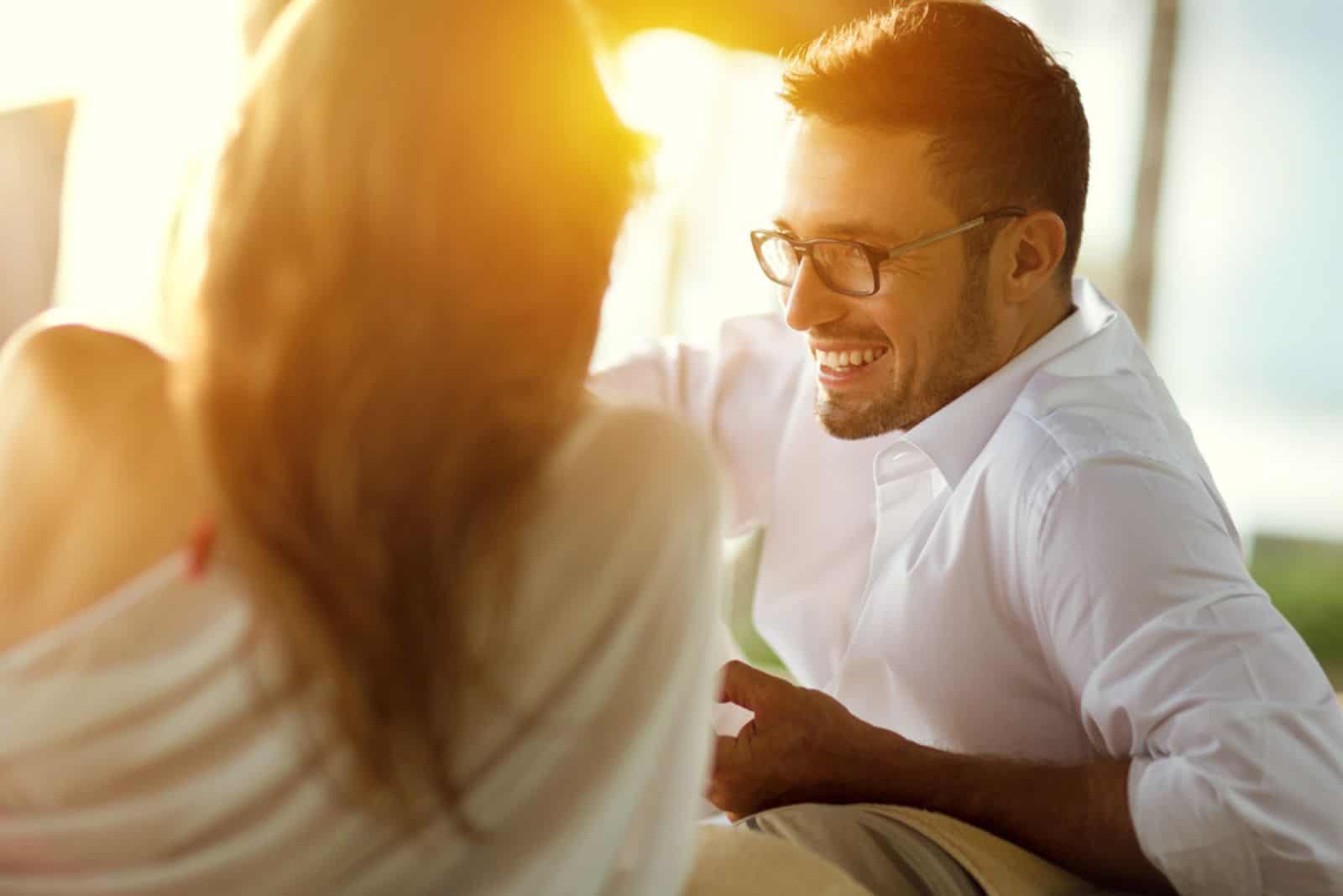 un homme souriant avec des lunettes est assis à côté d'une femme et ils parlent