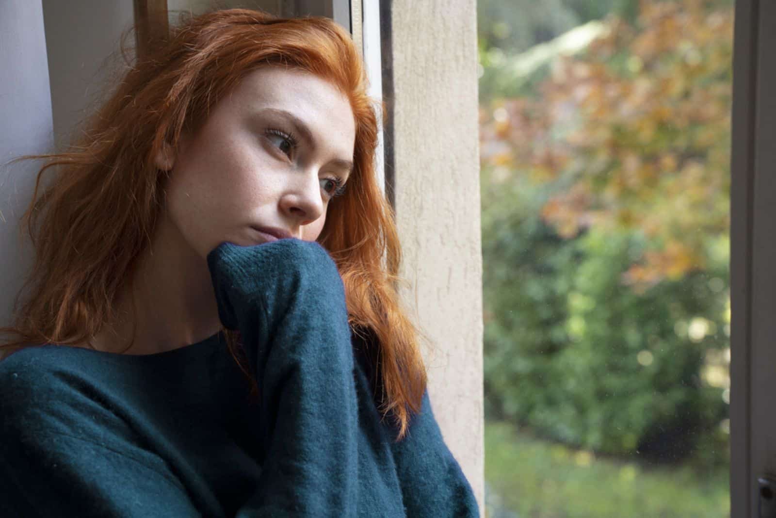 une fille aux cheveux roux est assise près de la fenêtre