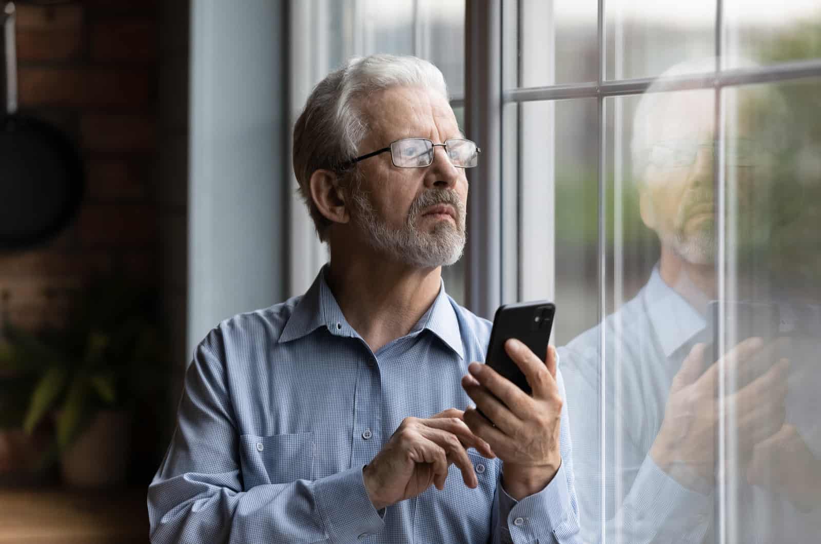 homme plus âgé tenant son téléphone tout en regardant par la fenêtre