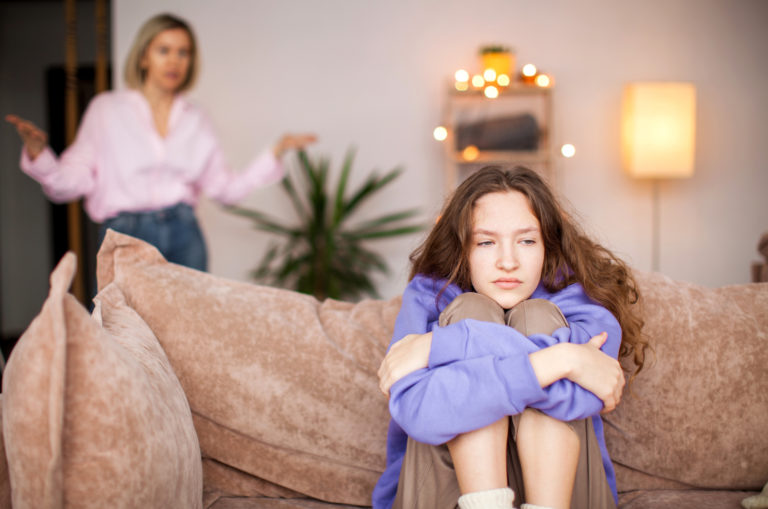 fille triste assise sur un canapé avec une mère criant en arrière-plan