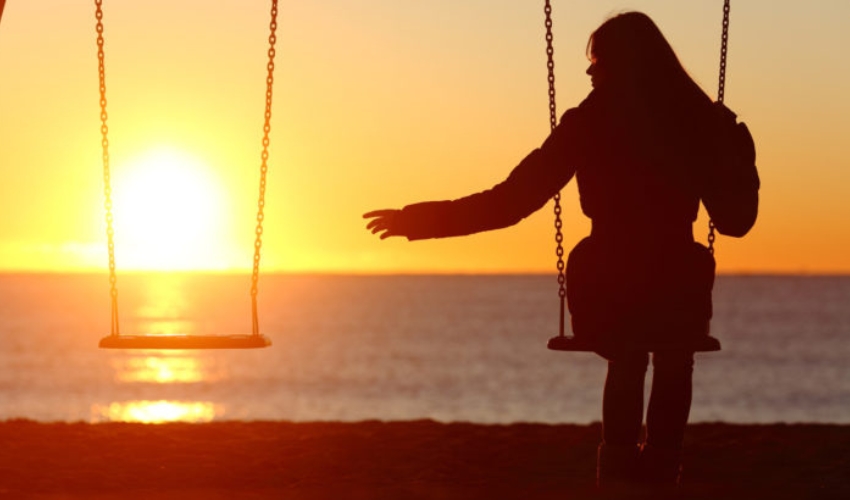 Femme celibataire seule manquant un petit ami en se balançant sur la plage au coucher du soleil