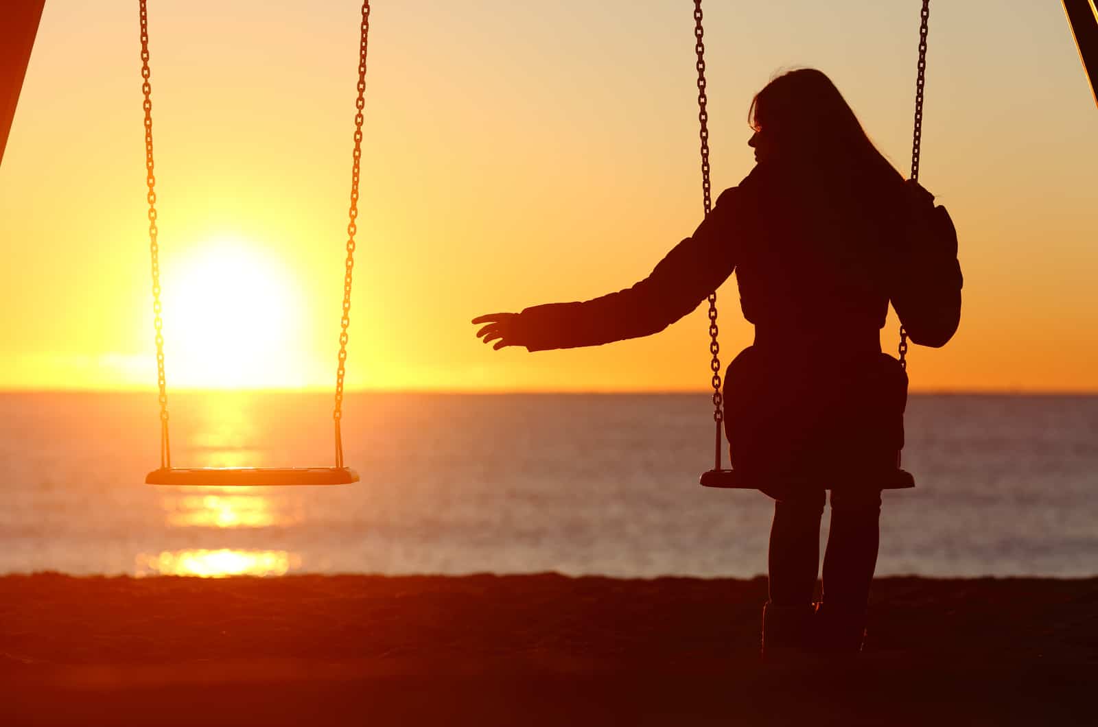 Femme célibataire seule manquant un petit ami en se balançant sur la plage au coucher du soleil