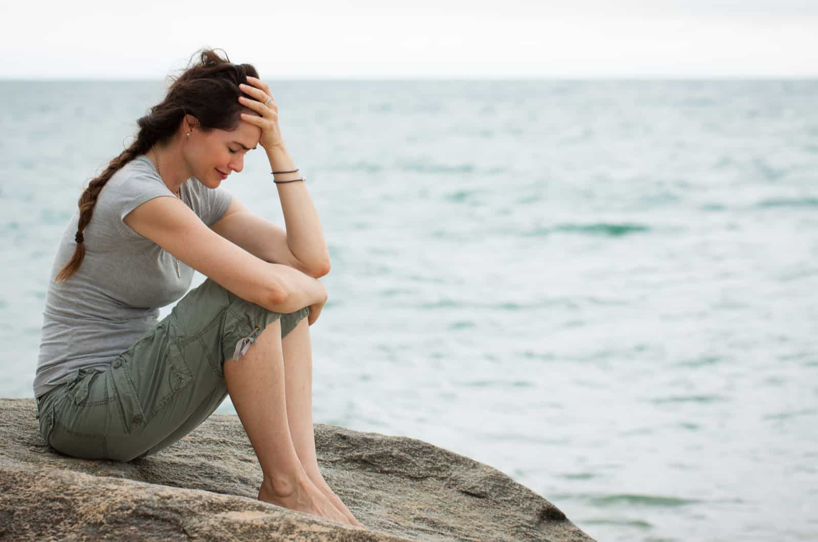 Femme bouleversée assise au bord de l'océan pleurant la tête dans la main