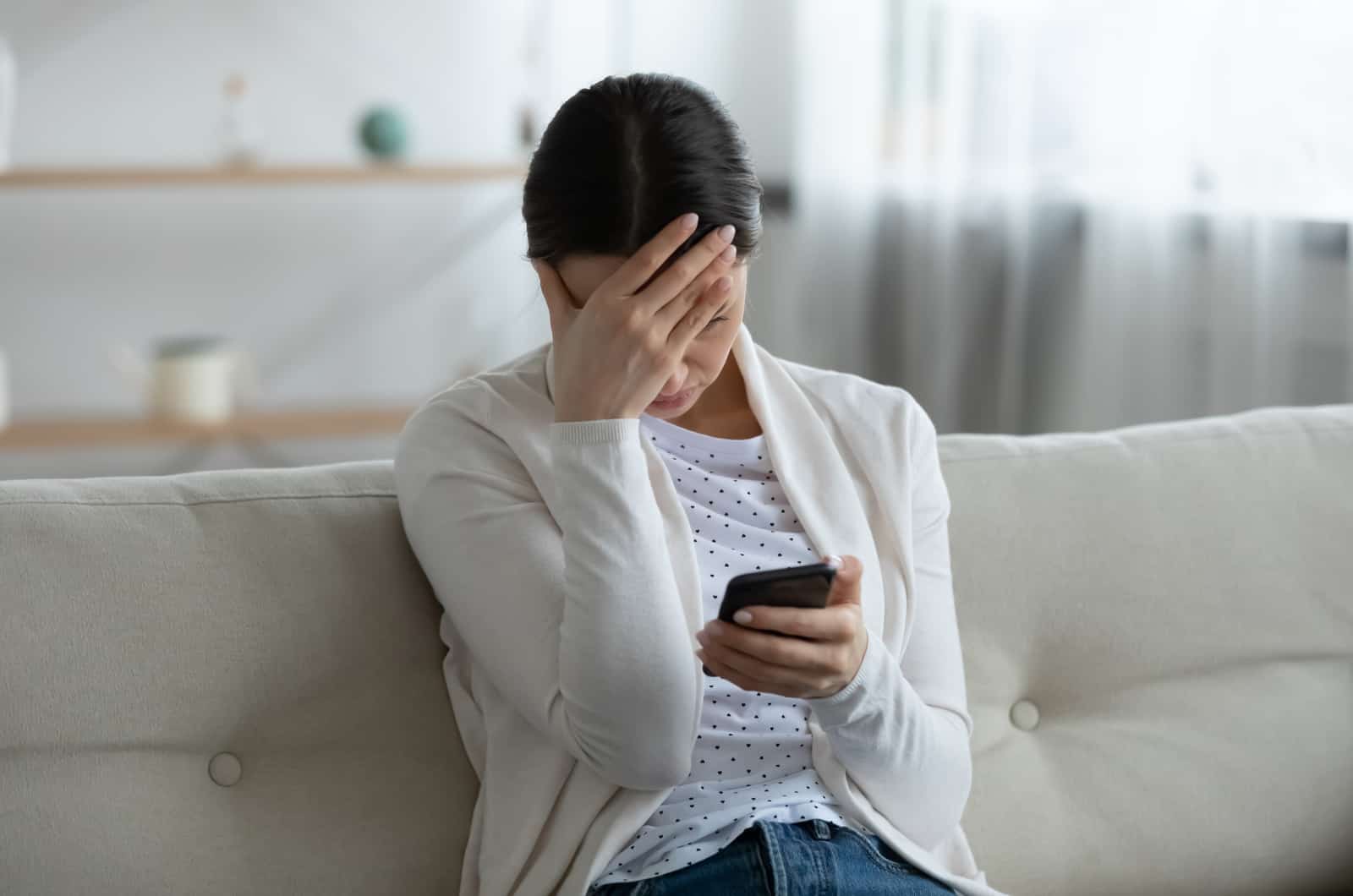 femme inquiète assise sur un canapé tenant son téléphone