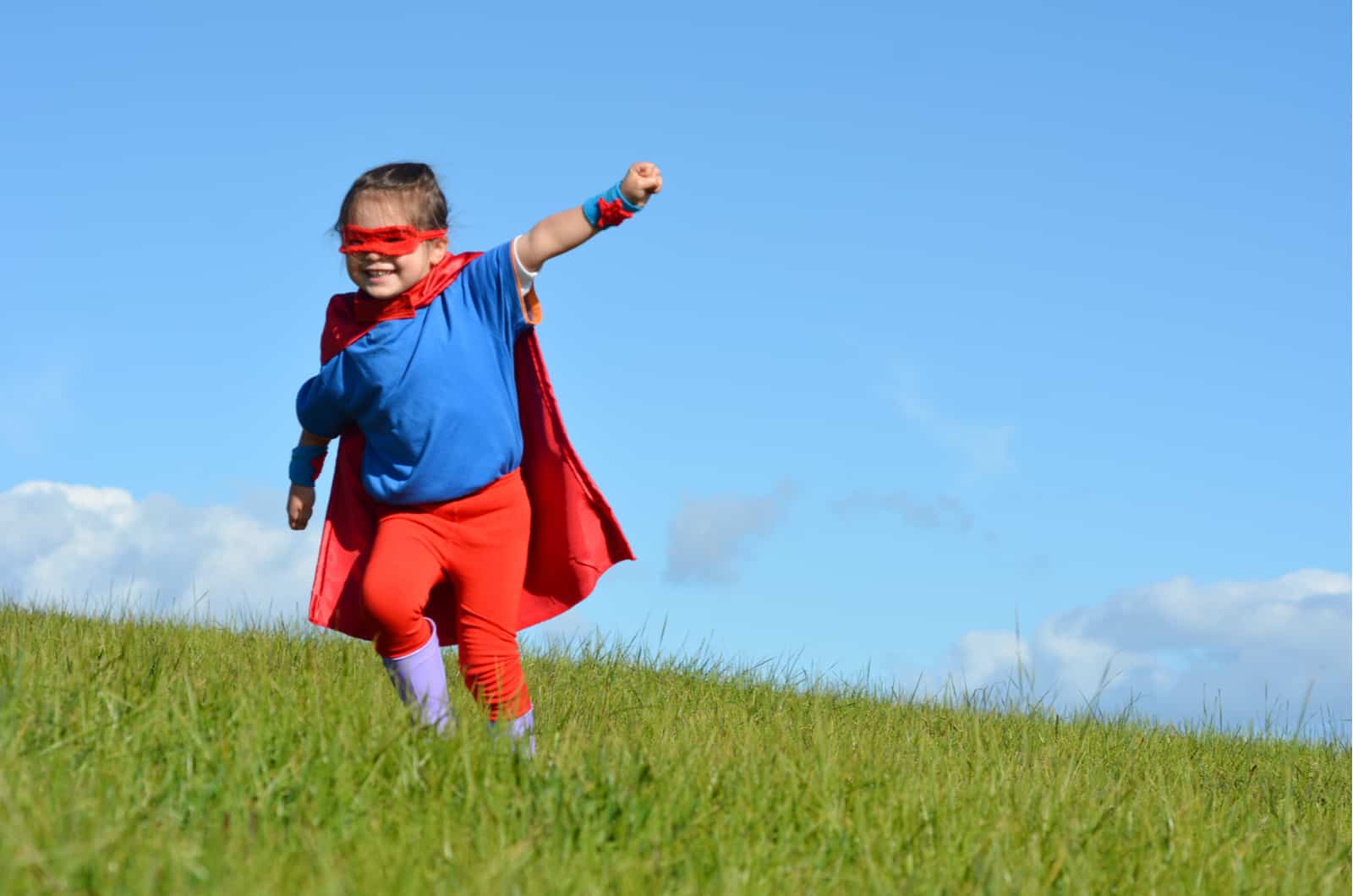 petite fille qui court dans le champ habillée en super-héros